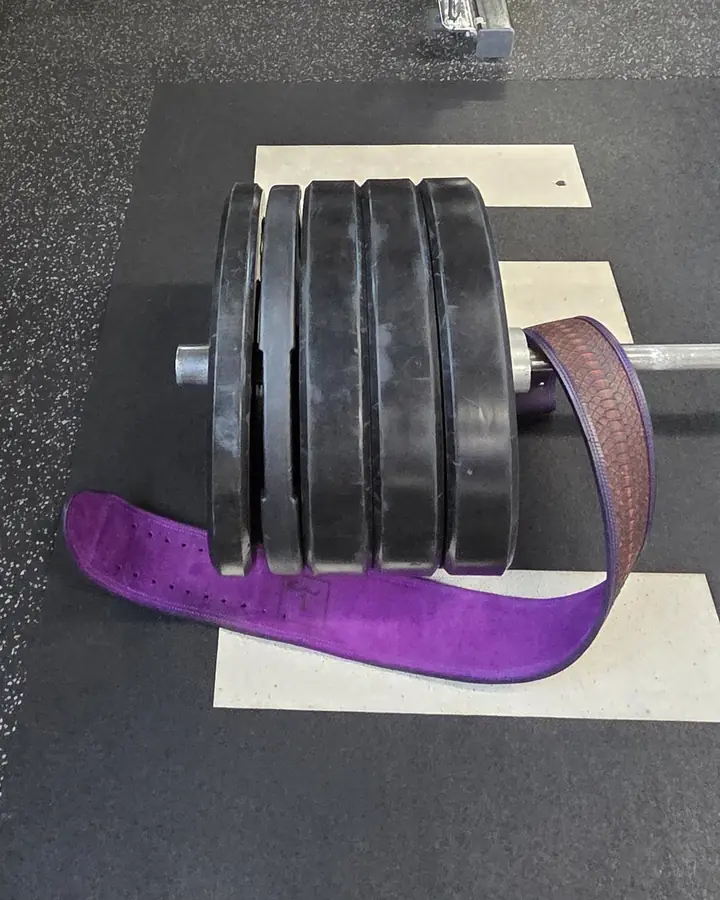 A purple lifting belt draped over a stack of weight plates on a gym platform