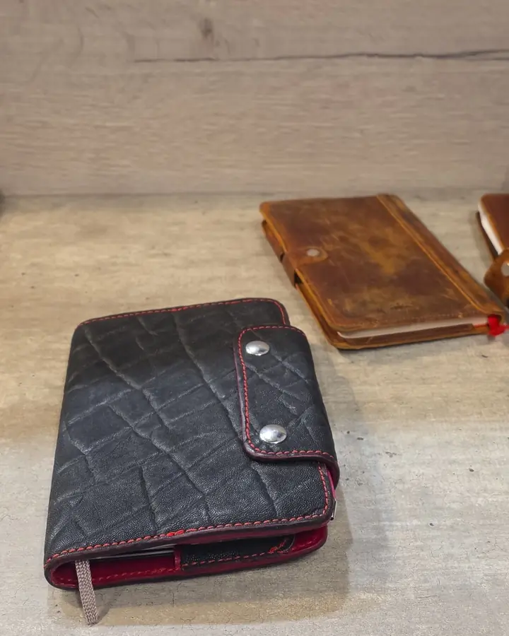 A worn black textured leather journal on a shelf next to a brown leather journal