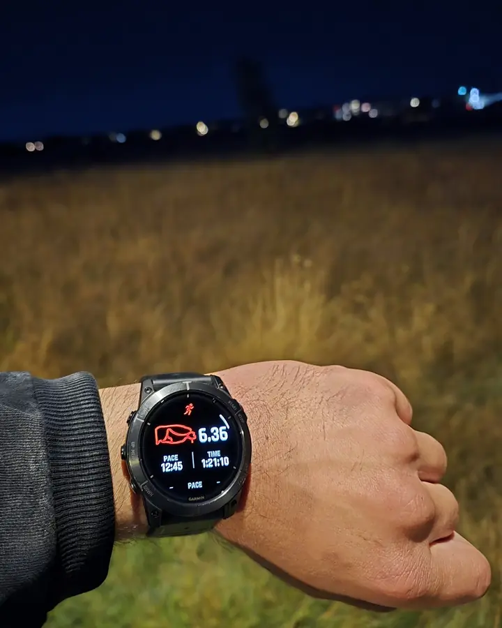 A wrist with a GPS watch showing a 6.36-mile run, held over a grassy field before sunrise